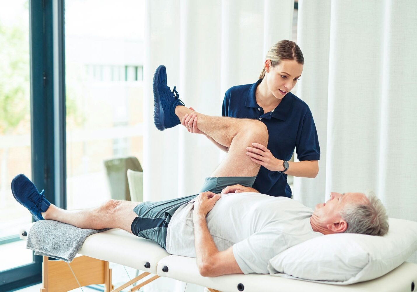 Therapist moving an older adult’s leg on a treatment table to improve joint mobility for daily activities.