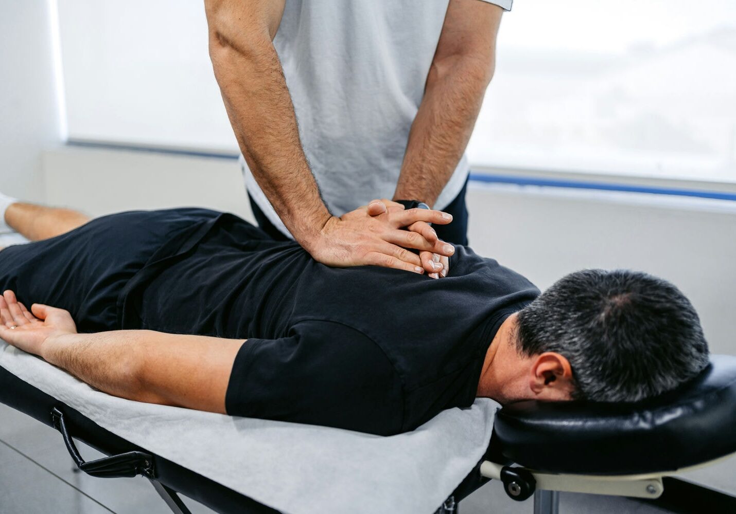 Chiropractor aligning patient’s spine during back adjustment session.