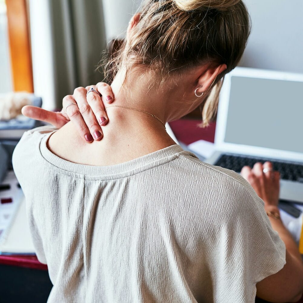 Person at a laptop massaging an aching neck, highlighting the need for ergonomic adjustments.
