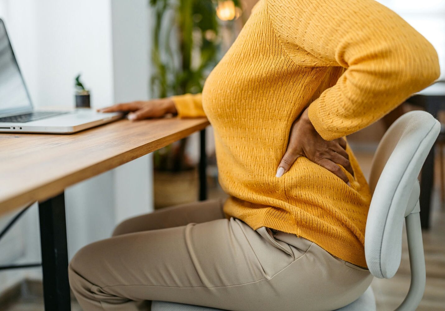 Seated individual holding the lower back at a desk, showing discomfort from extended sitting.