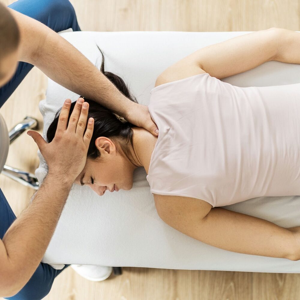 Female patient receiving neck manipulation from chiropractor on treatment table.