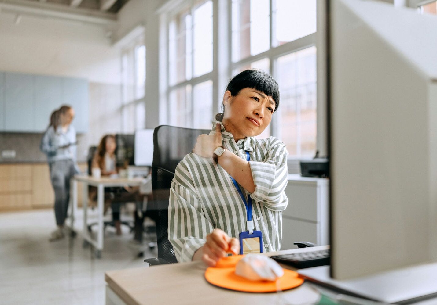 Office worker at a desktop workstation rubbing the neck due to prolonged sitting and poor ergonomics.
