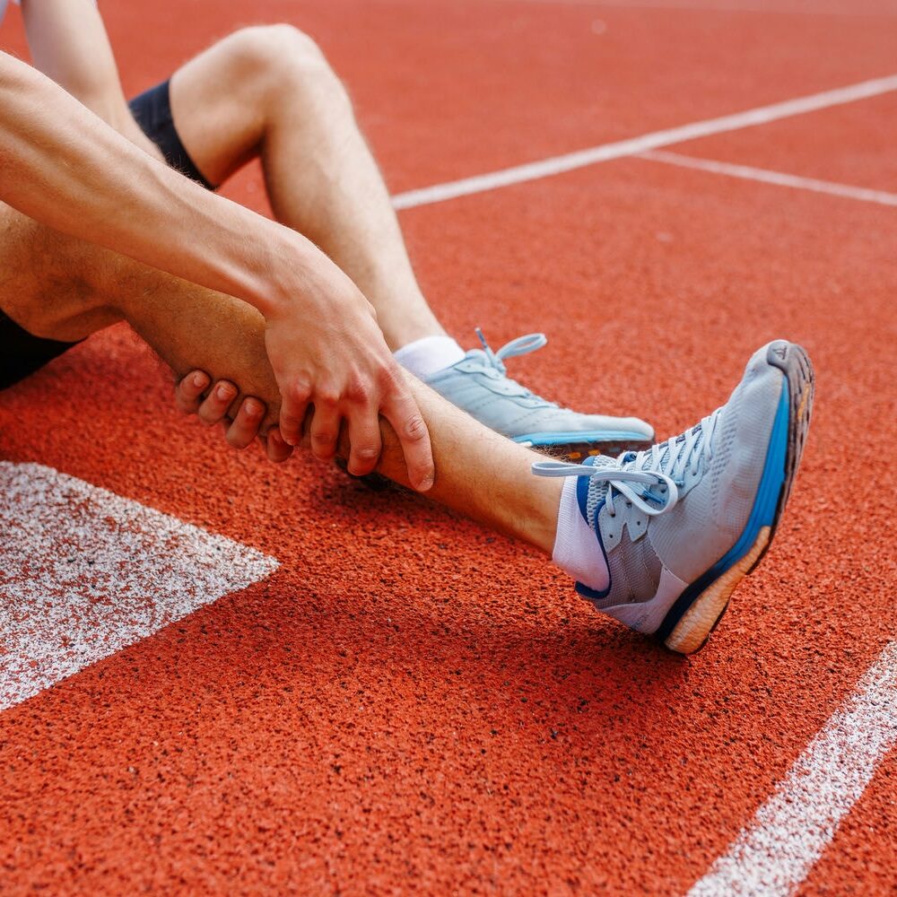 Close-up of an athlete holding a painful ankle after twisting it on the running track.