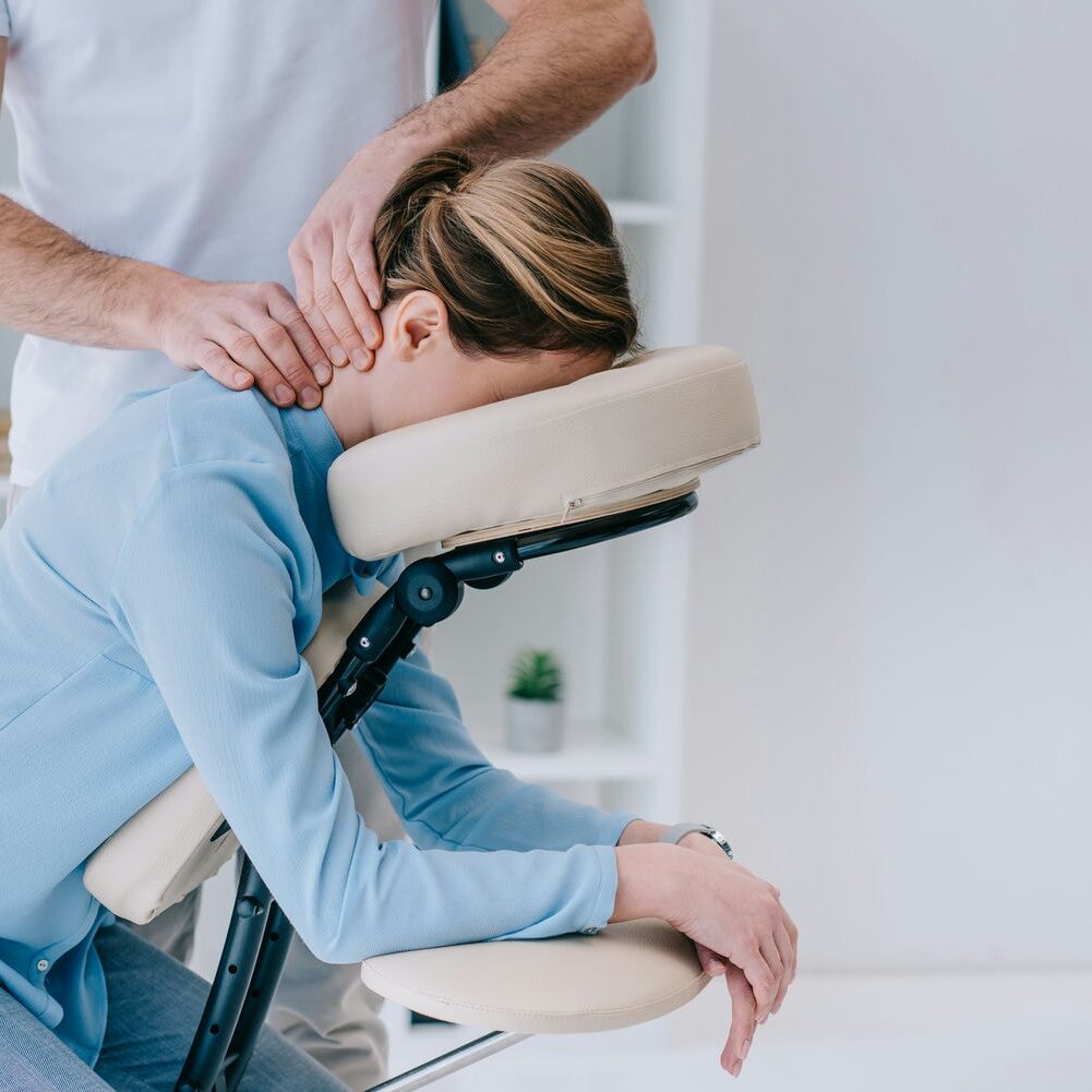 Client receiving a neck and shoulder massage while seated in a massage chair.