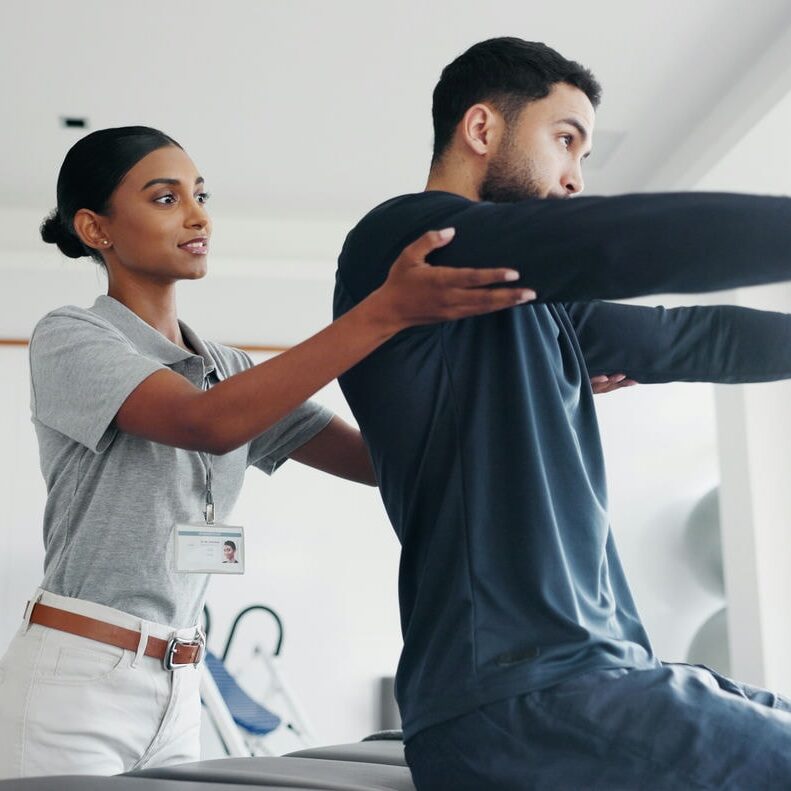 Therapist guiding a client through standing arm extension work to improve shoulder strength and functional reach.