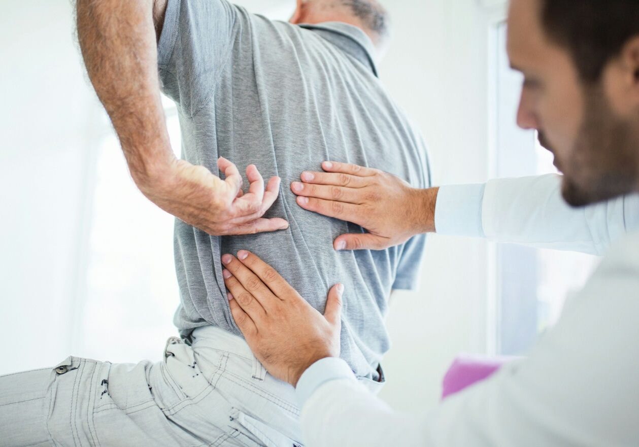 Patient holding the lower back while a clinician supports the torso during pain-relief care.