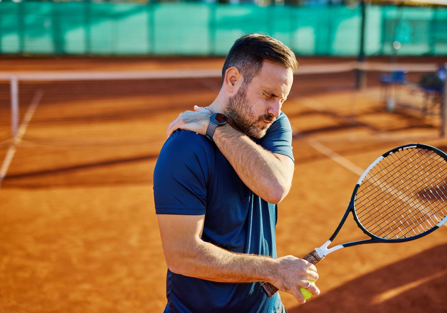 Tennis player clutching the shoulder while holding a racquet, indicating a sports-related shoulder injury.